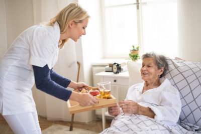 young health visitor bringing breakfast to a sick senior women